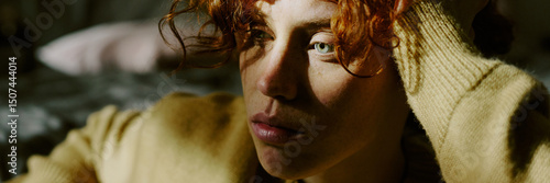 Obraz na plátně Young woman with curly red hair gazing thoughtfully, with sunlight highlighting her features