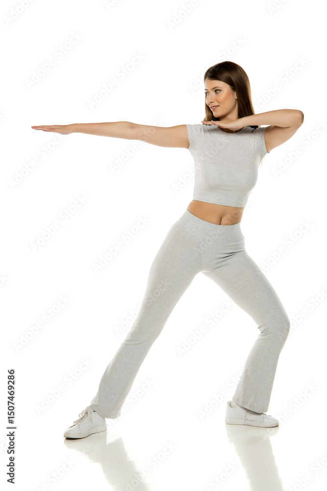 Sporty young woman in action pose, stretching arms in studio, gray outfit, white background. Sporty young woman in action pose, stretching arms in studio, gray outfit, white background.