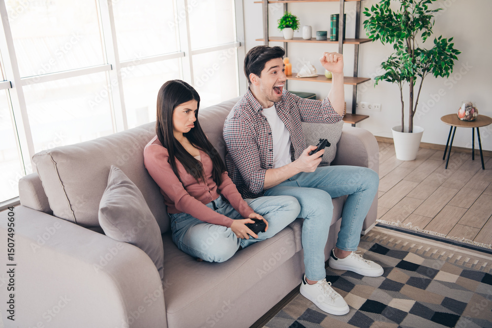 Fototapeta premium Young couple enjoying leisure time at home with a video game, showing emotions and bonding in a cozy living room setting