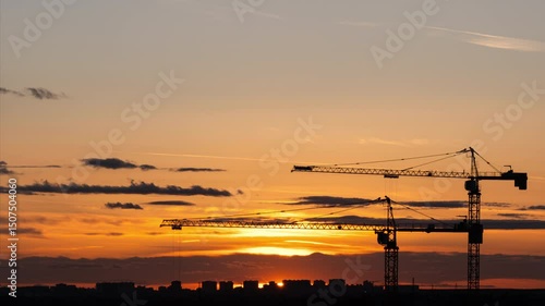 Time lapse. Urban landscape at night time. Close-up video of construction site with silhouettes of two working cranes on the breathtaking sunset background