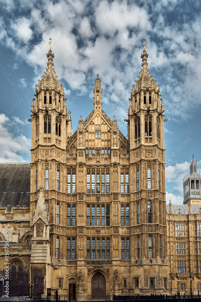 Fototapeta premium Majestic Palace of Westminster in London, highlighting Gothic architecture with intricate stonework and tall towers under a partly cloudy sky. A historic landmark in the heart of the city.