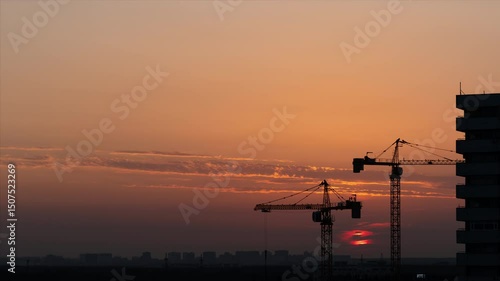 Time lapse of two working construction cranes on the fantastic sunset background. Night urban skyline