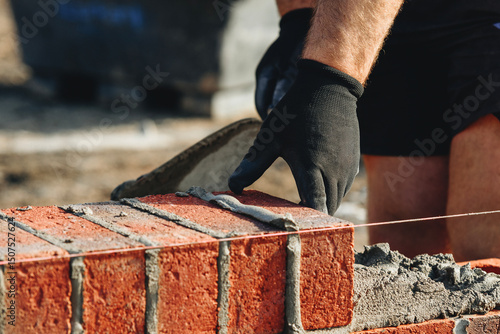 Schilderij op canvas Close-up of skilled bricklayer working on construction site laying red bricks fo