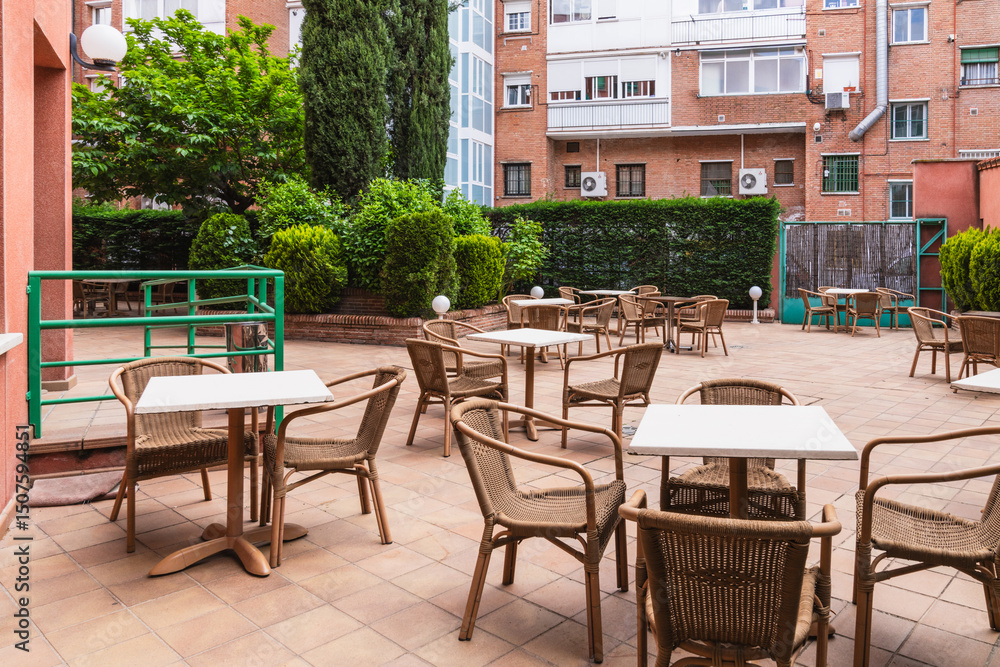 Obraz premium Wicker chairs and white tables standing on tiled patio in tranquil garden of nursing home, offering peaceful outdoor space
