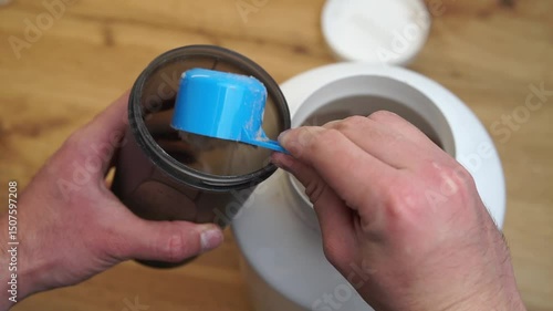 Close up of a man preparing protein shake. Pouring chocolate protein powder in a shaker