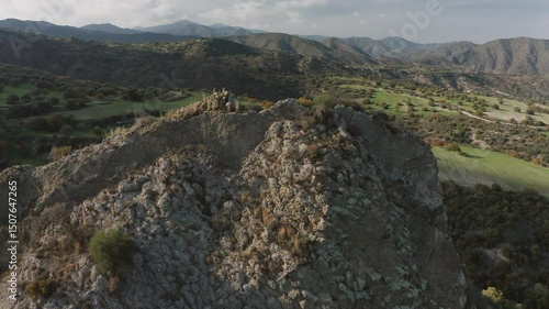 Sunlight illuminates a rocky peak overlooking a lush green valley in the mountains of Cyprus