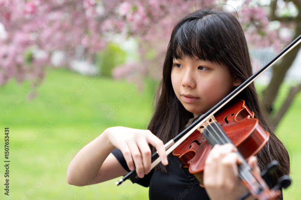 A young teenage girl plays the violin with focus under blooming cherry blossom trees, blending musical artistry with the serenity of springtime. A young teenage girl plays the violin with focus under blooming cherry blossom trees, blending musical artistry with the serenity of springtime.