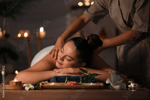 Beautiful young woman getting massage in dark spa salon
