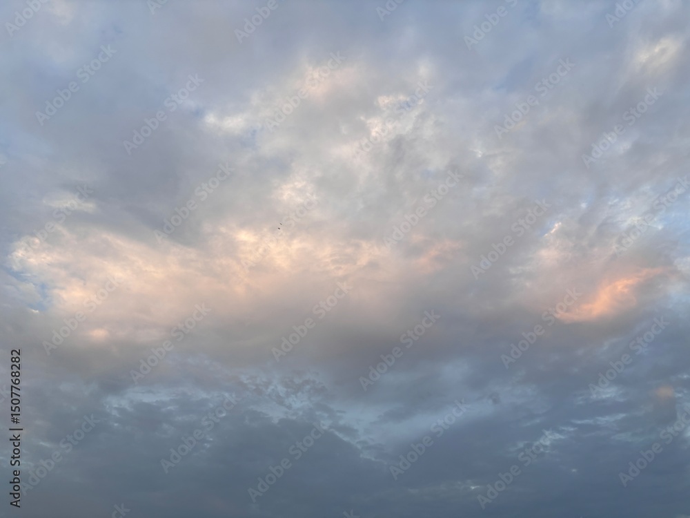 Obraz premium The expansive sky is dominated by soft, layered cloud formations, featuring varying shades of gray, white, and a touch of orange, perfect as a calming backdrop, for projects that require natural