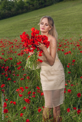 Attractive young woman in a beige dress sitting in a blooming poppy field on a sunny day. Concept of femininity, serenity, connection with nature, rural elegance, seasonal flowers and summer vibes.