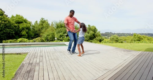 African American, Father and daughter dancing joyfully on wooden deck in sunny backyard