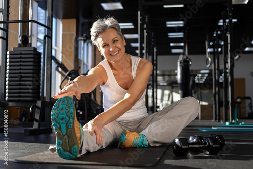 Athletic fitness elderly gray-haired woman stretching body at gym enjoy physical exercise activity.