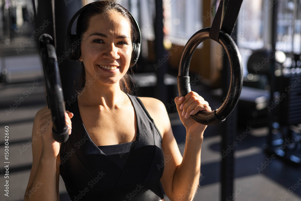Obraz premium Young beautiful Asian woman doing fitness exercises on sports rings in the gym.