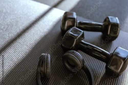 Black dumbbells for sports and acoustic headphones lie on the floor in the gym on a stylish yoga mat