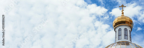 Golden onion dome of an Orthodox church under a blue sky with clouds. Architecture with white walls and gilded cross. Religious traditions and design of the church in Russian style.