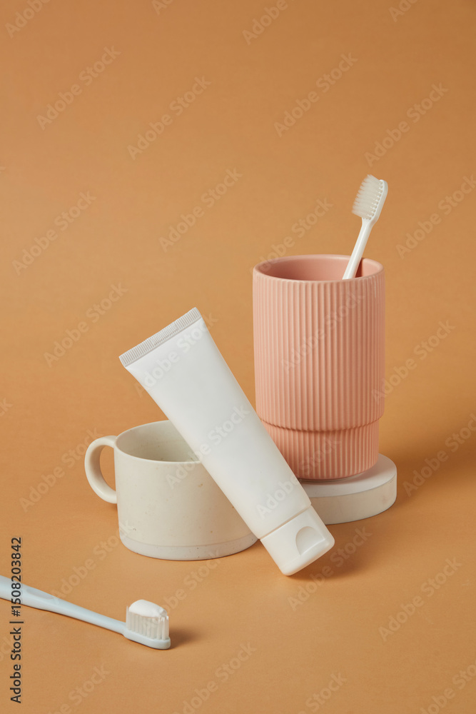 Obraz premium Muted coral cup holding oral care items, placed in a centered vertical frame. The scene is sparse, symmetrical, and bathed in soft light, enhancing the minimalist while maintaining product clarity.