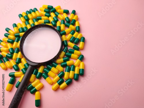 Medicine pill and magnifying glass on a pink background with copy space