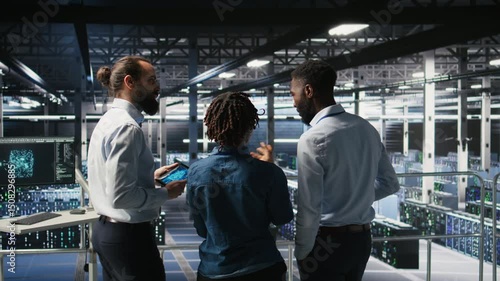 Data center manager talking with workers performing maintenance on supercomputers used for AI. Server hub team leader and staff members upgrading rigs used for deep learning training, camera A
