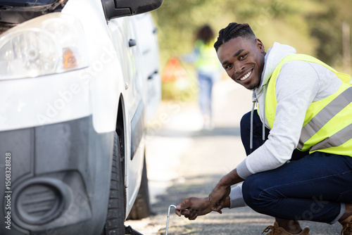 young man changing the punctured tyre on his car