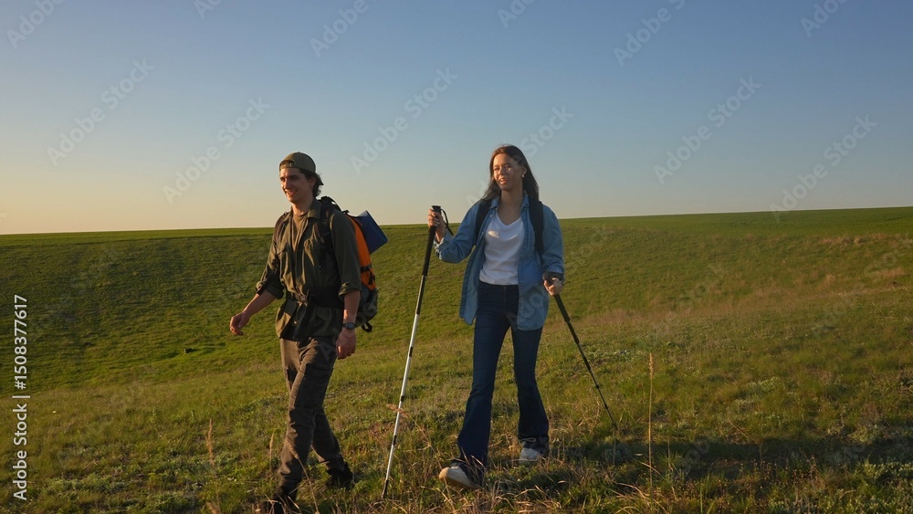 Young Couple Hiking with Trekking Poles in Open Green Field Young Couple Hiking with Trekking Poles in Open Green Field