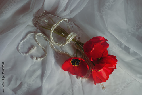 A bouquet of red tulips, entwined with a pearl thread, on a white airy fabric.
