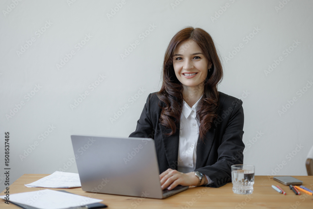 Professional woman working at desk with laptop and smiling brightly during office hours Professional woman working at desk with laptop and smiling brightly during office hours