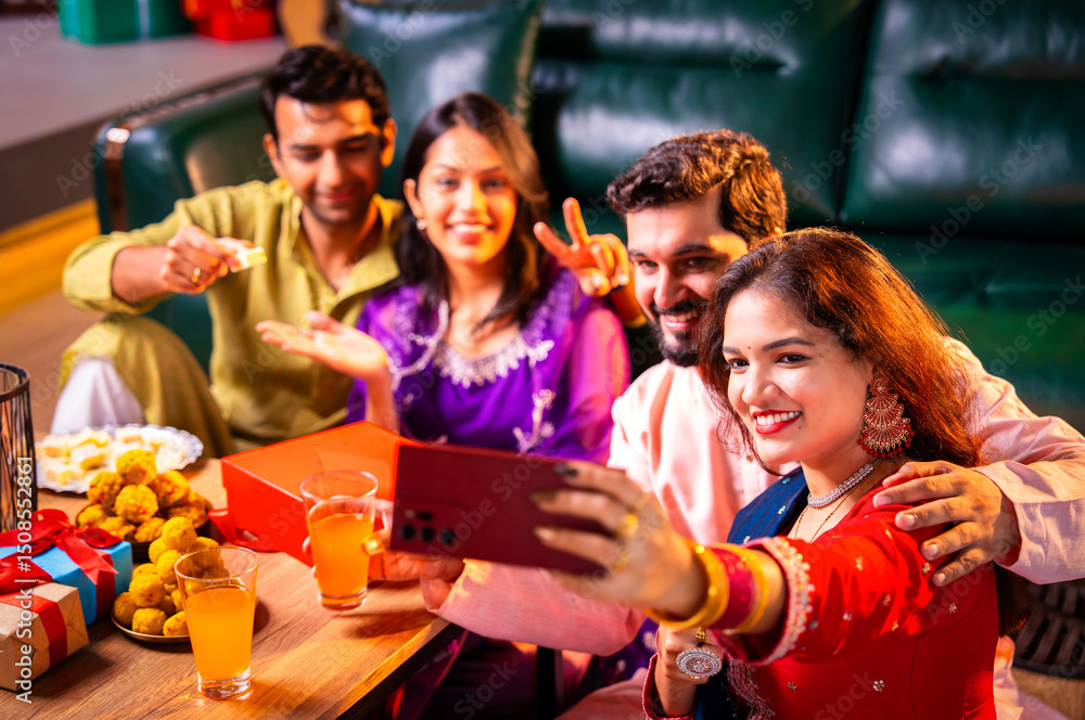 Obraz premium Smiling and clicking festive selfie while holding Diwali sweets with family and friends at home