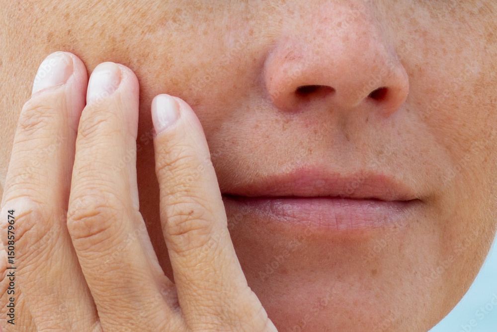 Obraz premium Woman touching her cheek with fingers showing natural skin texture and freckles