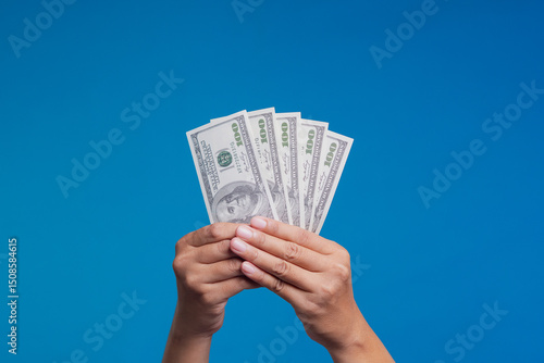 Fotografija Hands holding fan of US dollar bills on blue background, concept of wealth, savings, and finance