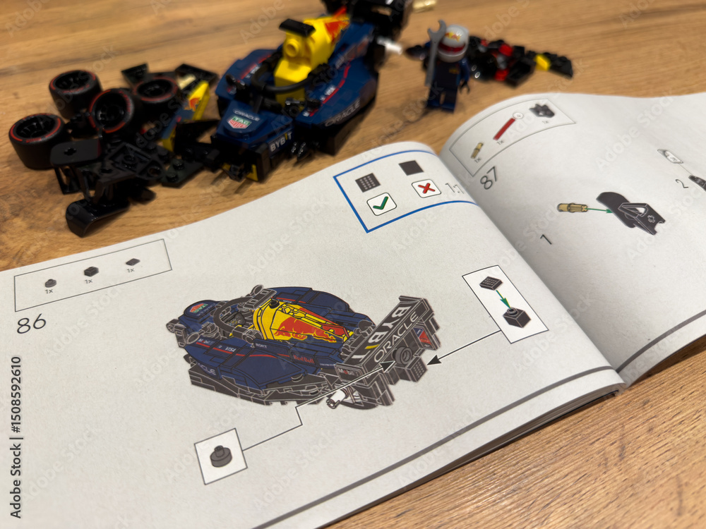 Fototapeta premium Moscow, Russia, April 26, 2025: LEGO Speed Champions Red Bull Racing Formula 1 car partially assembled, shown next to step by step instructions and scattered LEGO parts on a wooden surface