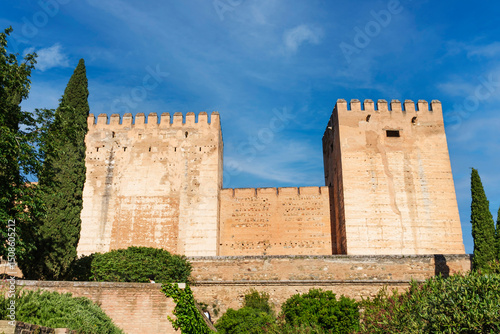 View of the outer wall and fortified towers of the Alhambra in Granada, with daylight and blue sky.