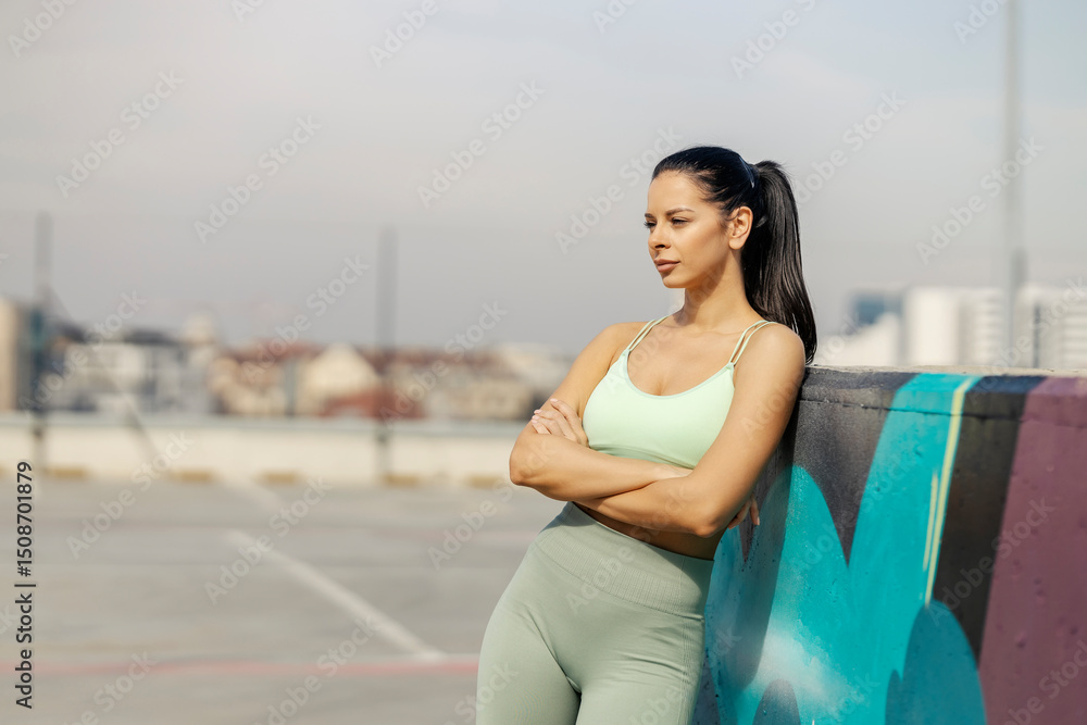 Fototapeta premium Portrait of confident street runner leaning on a wall and taking a break from city fitness.