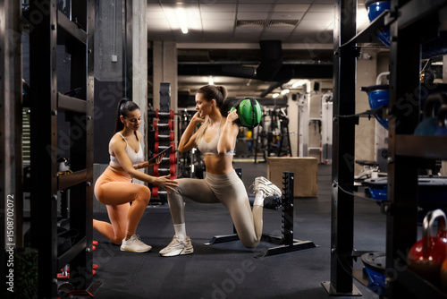 фотографія Full length of fit strong sportswoman doing bulgarian split squats with weight bag on shoulders at gym with personal trainer