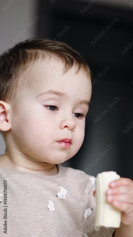 Little kid is eating holding food in both hands. Lovely baby boy eating banana. Low angle view. Vertical video Little kid is eating holding food in both hands. Lovely baby boy eating banana. Low angle view. Vertical video