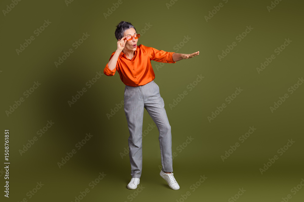 Middle aged woman in casual stylish attire striking a playful pose against a solid khaki green background Middle aged woman in casual stylish attire striking a playful pose against a solid khaki green background