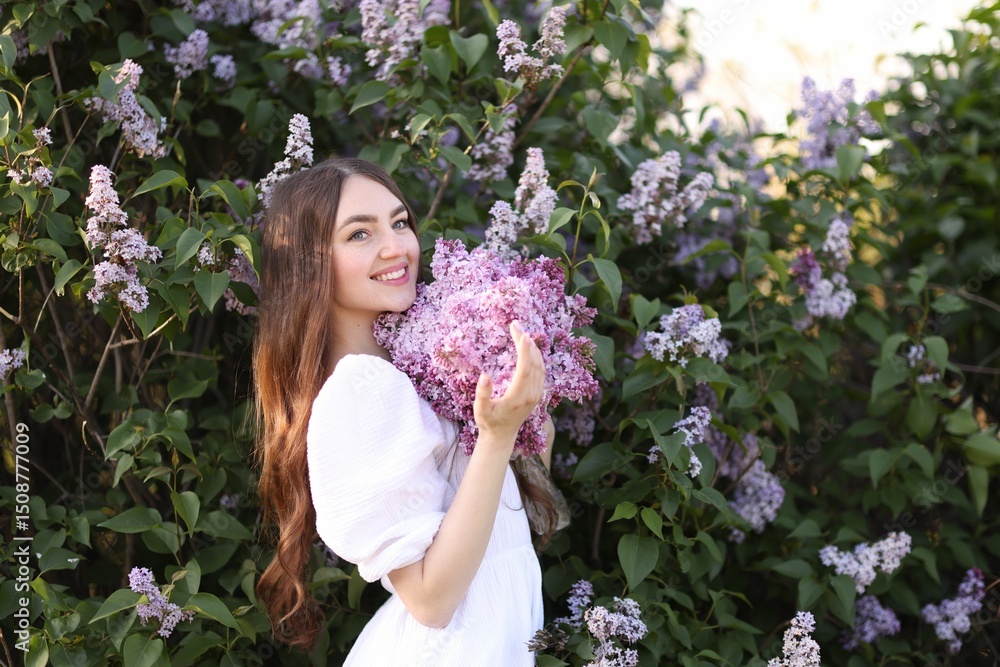 Fototapeta premium Smiling woman among lilac flowers and leaves outdoors
