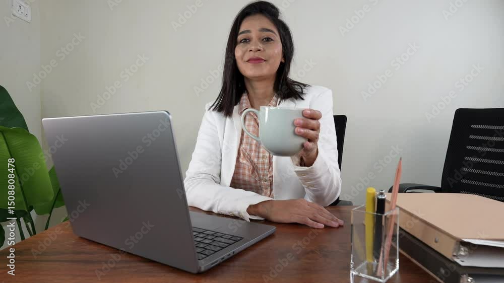 woman offering cup of tea to the camera, she is sitting in office with open laptop and files woman offering cup of tea to the camera, she is sitting in office with open laptop and files