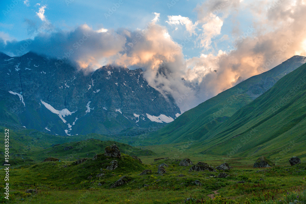 Fototapeta premium mountain landscape with clouds und green grass at sunset
