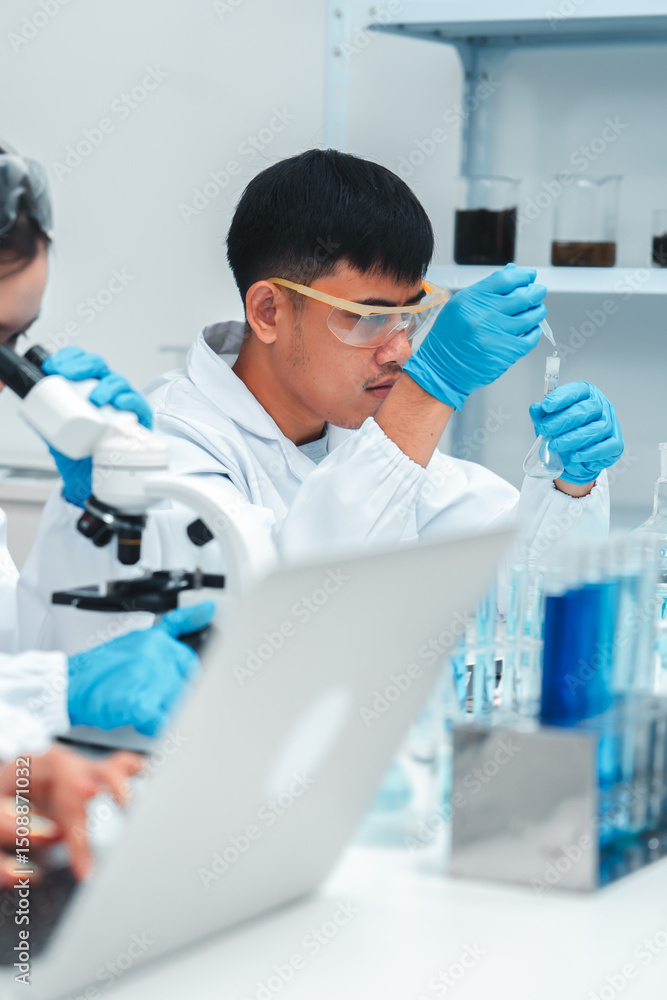 Young scientists working together in a laboratory, one using a microscope and others recording data and typing on a laptop, representing modern teamwork in scientific research and education. Young scientists working together in a laboratory, one using a microscope and others recording data and typing on a laptop, representing modern teamwork in scientific research and education.