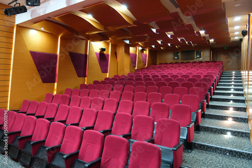 Elegant 100-Seat Auditorium with Red Chairs and Warm Yellow Lighting – Modern Seminar and School Hall Interior photo