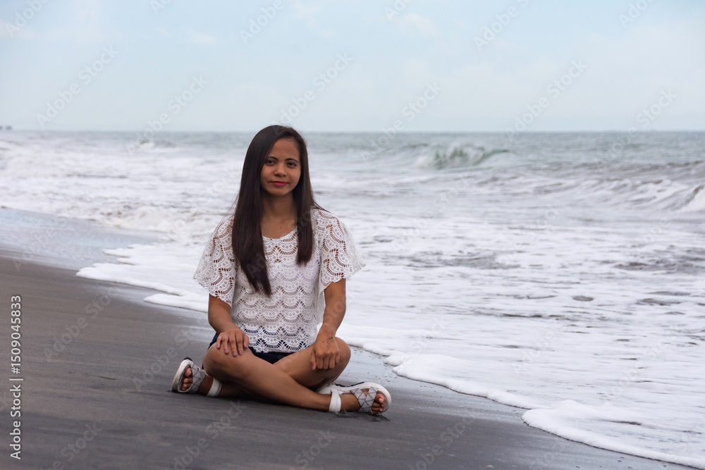 Fototapeta premium young woman sitting on wet black sand beach near waves