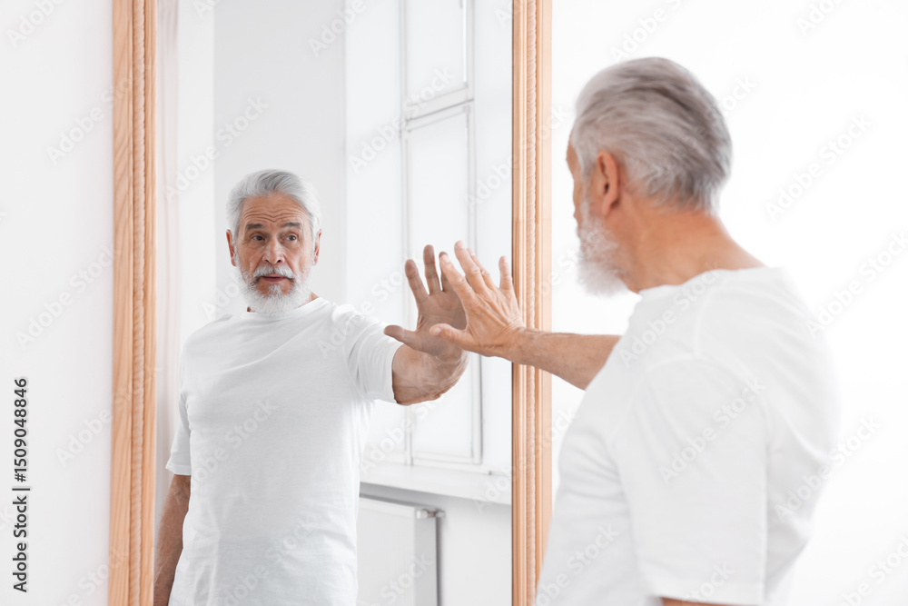 Obraz premium Handsome senior man looking at himself in mirror indoors