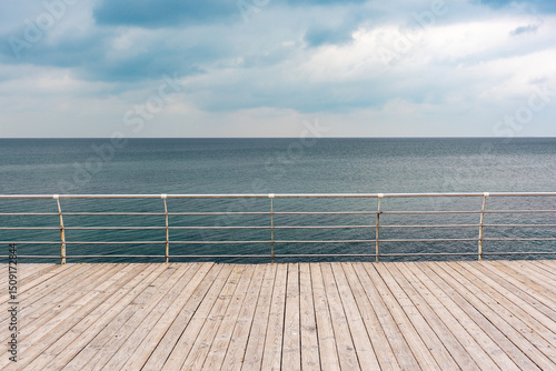 Obraz na plátně Empty seaside promenade with wooden decking and metal handrails on a cloudy day
