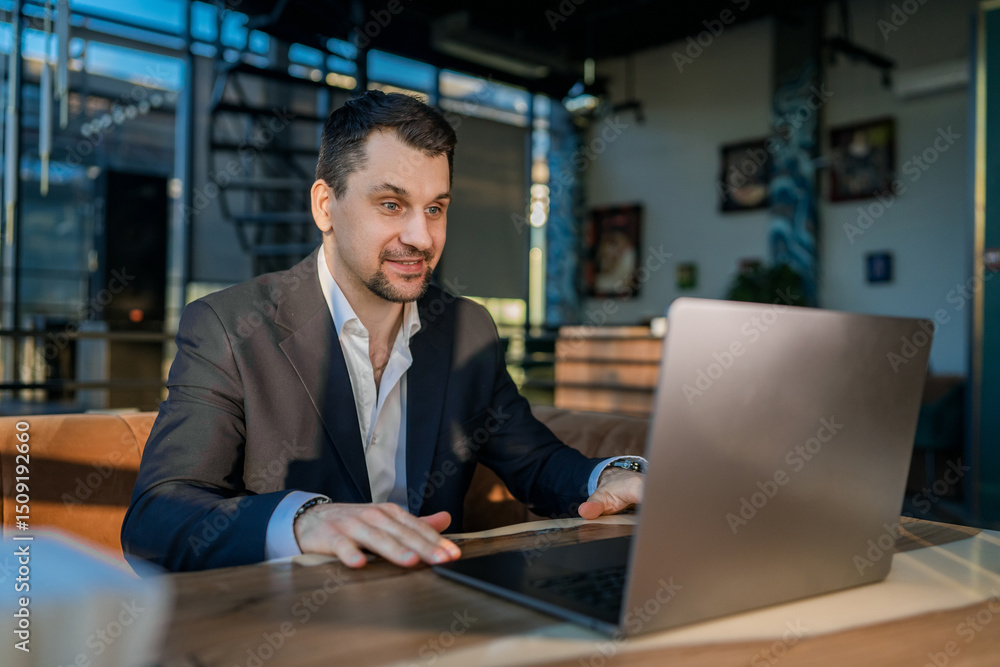 Fototapeta premium Businessman Engaged with Laptop in Modern Cafe Setting