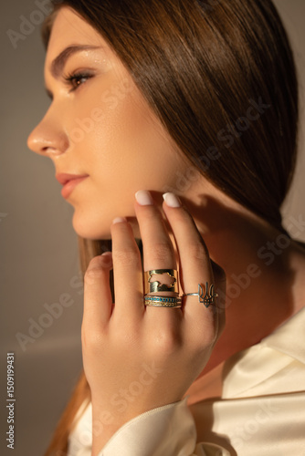 girl's face in profile, hand near face, rings with Ukrainian symbols on fingers