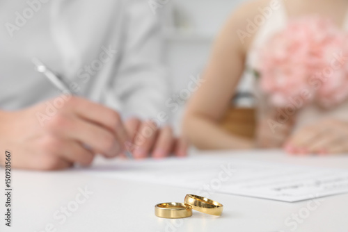 Fotografie Newlyweds signing marriage contract and wedding rings on desk, selective focus