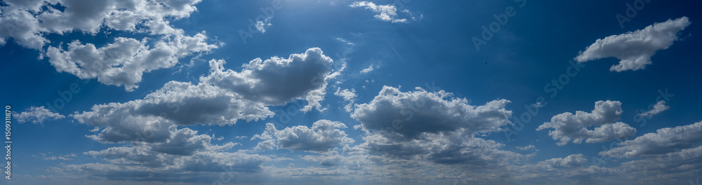 Obraz premium Panorama of a blue summer sky with fluffy white cumulus clouds a sun above the image 