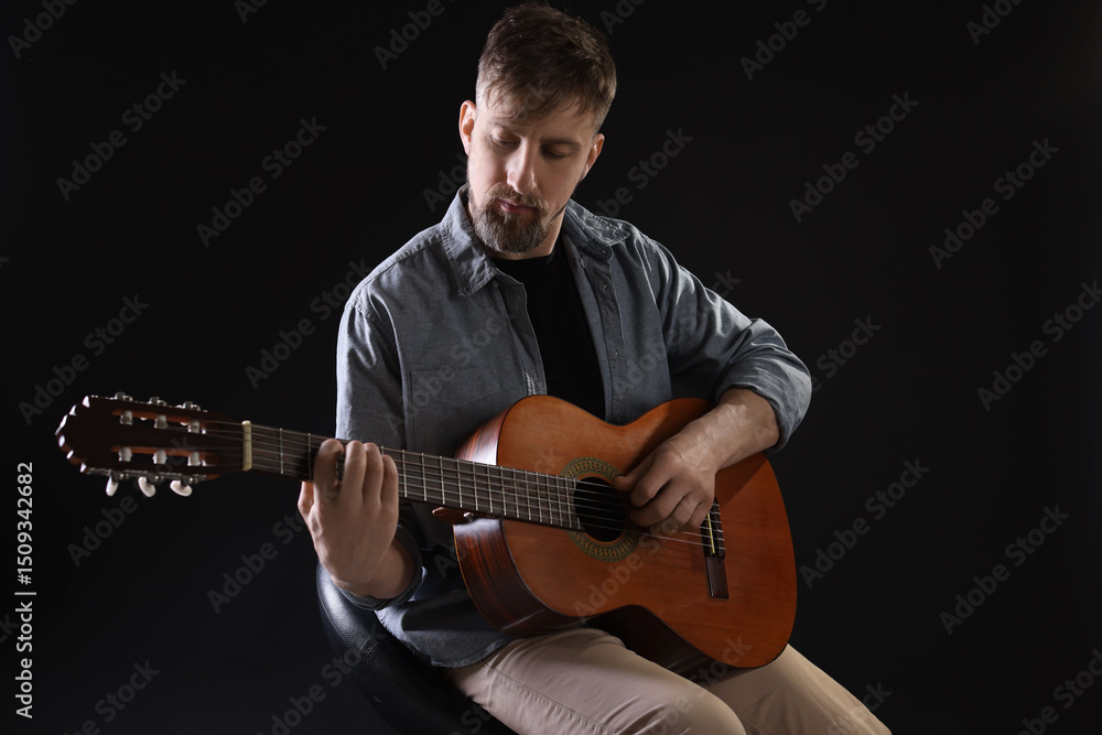 Obraz premium Man playing guitar on chair against black background