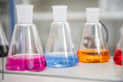 Three conical flasks filled with vibrant liquids are shown in close-up. The bright hues create a striking composition, emphasizing the beauty of scientific analysis and experimentation in the lab.