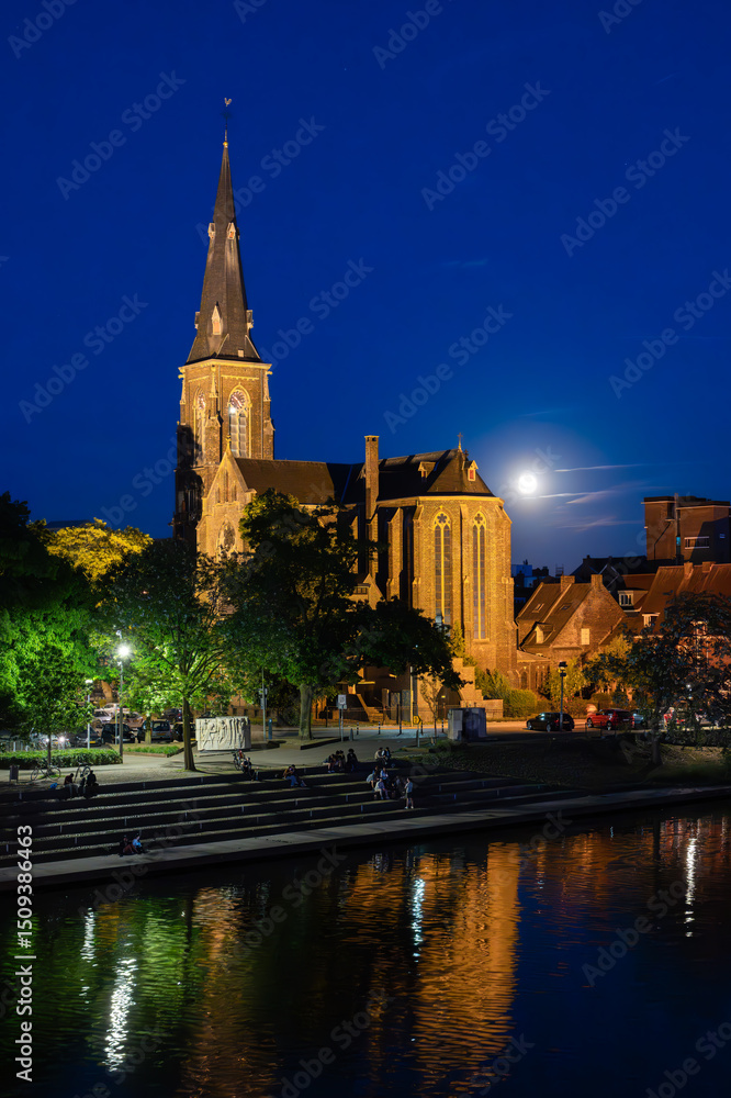 Naklejka premium Illuminated Historic Church by the River Maas in Maastricht at Night